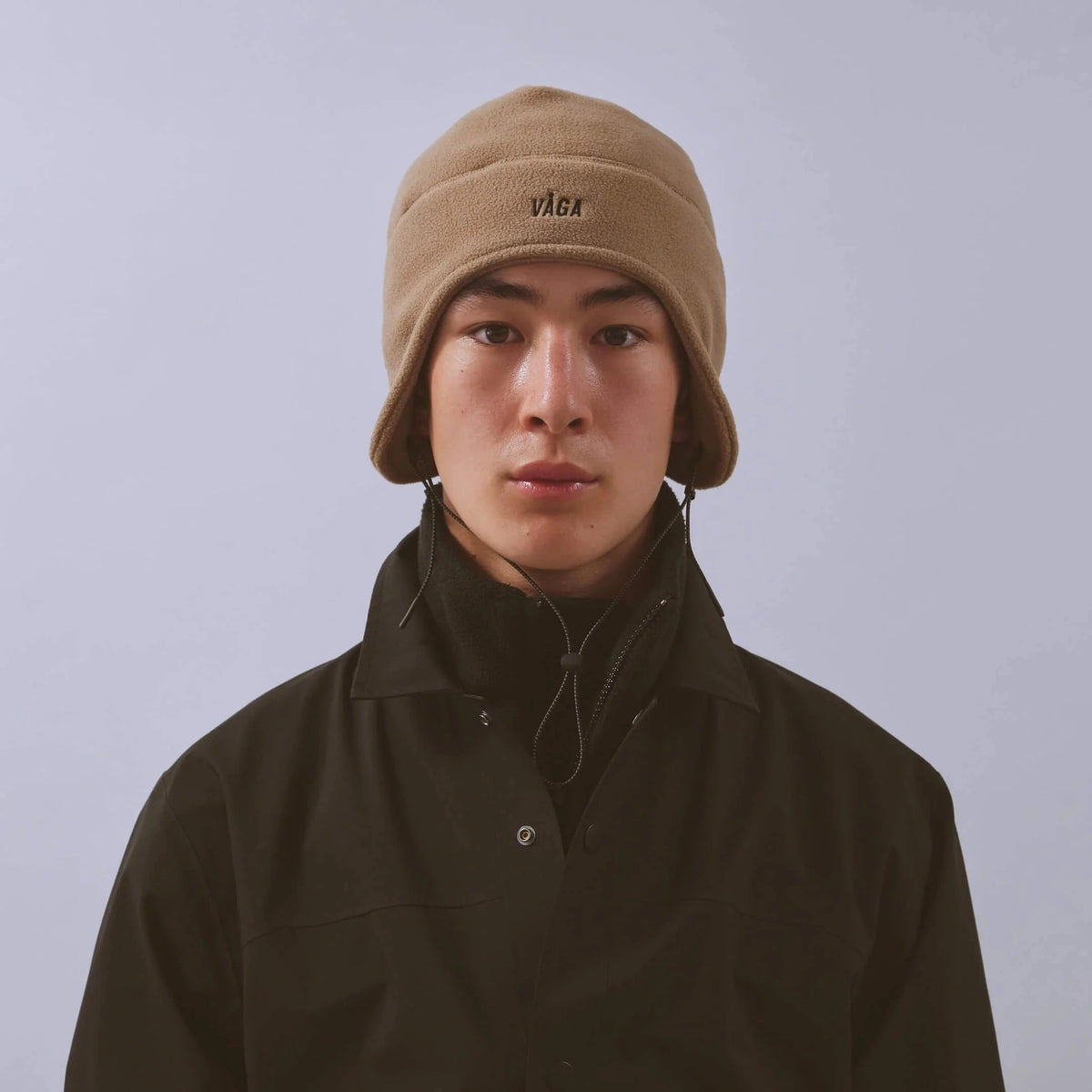 Våga Fleece Summit Beanie in taupe – gedragen, vooraanzicht met logo en oorflappen